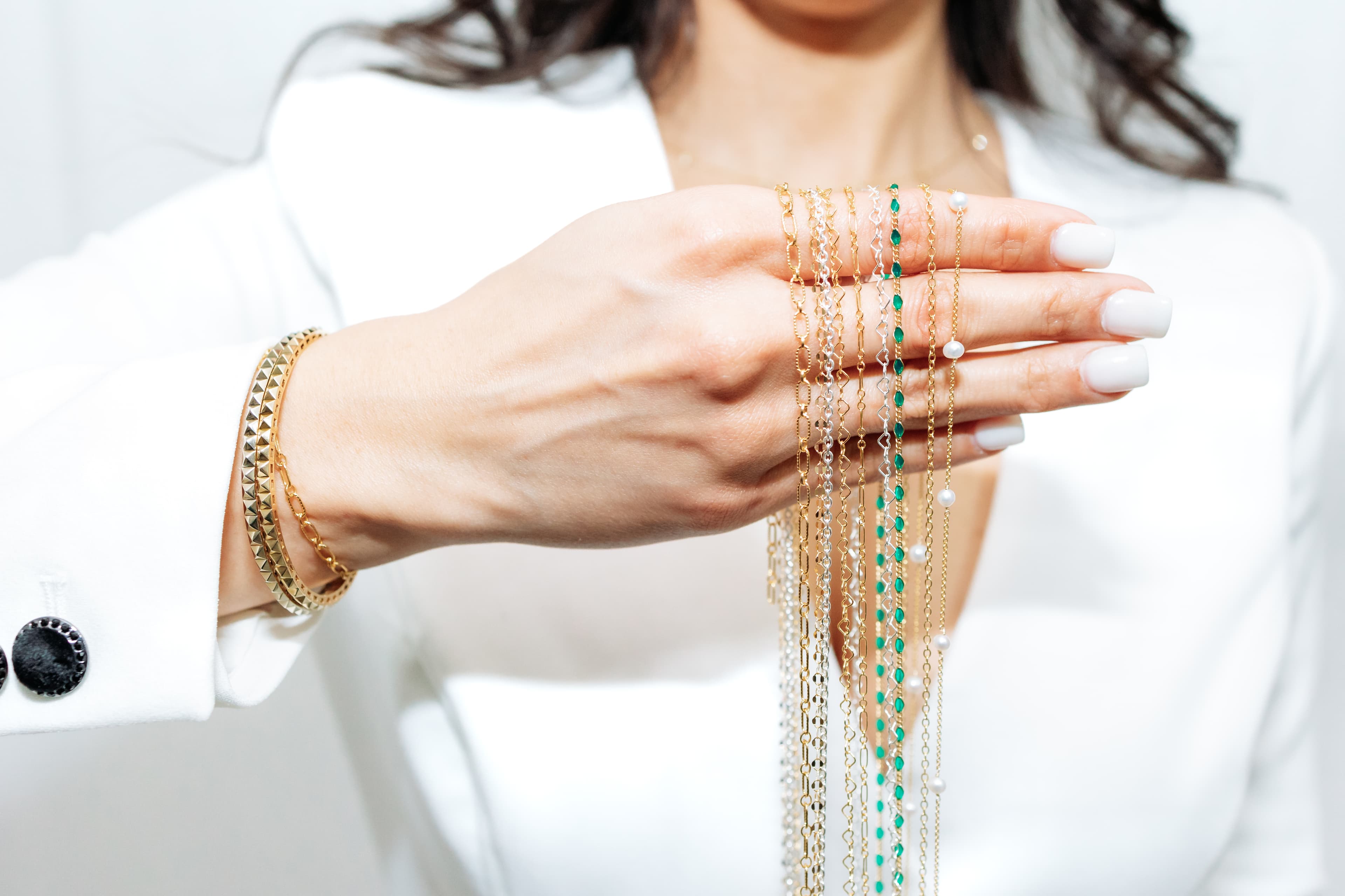 Hand holding permanent jewelry chains in gold, silver, and emerald